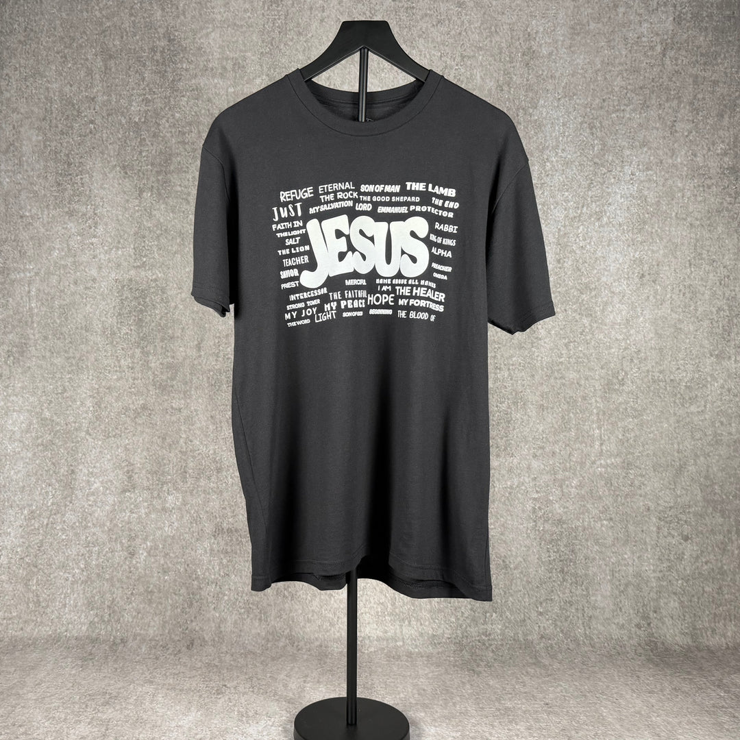 Black Christian t-shirt graphic designed by  Christ Centered Faith featuring the names of Jesus hanging with a gray background.